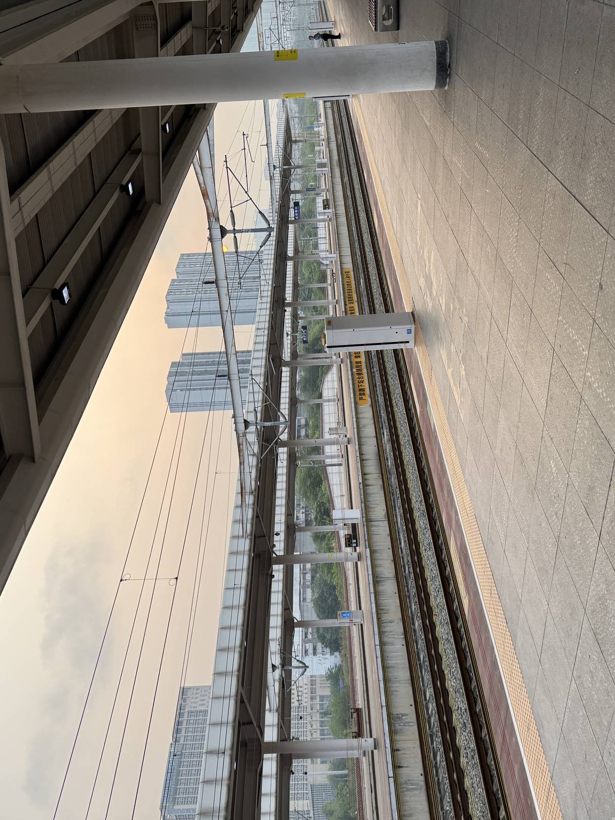 站台轨道全景，雨棚、白色支柱、铁轨与接触网，远处城市建筑倒影