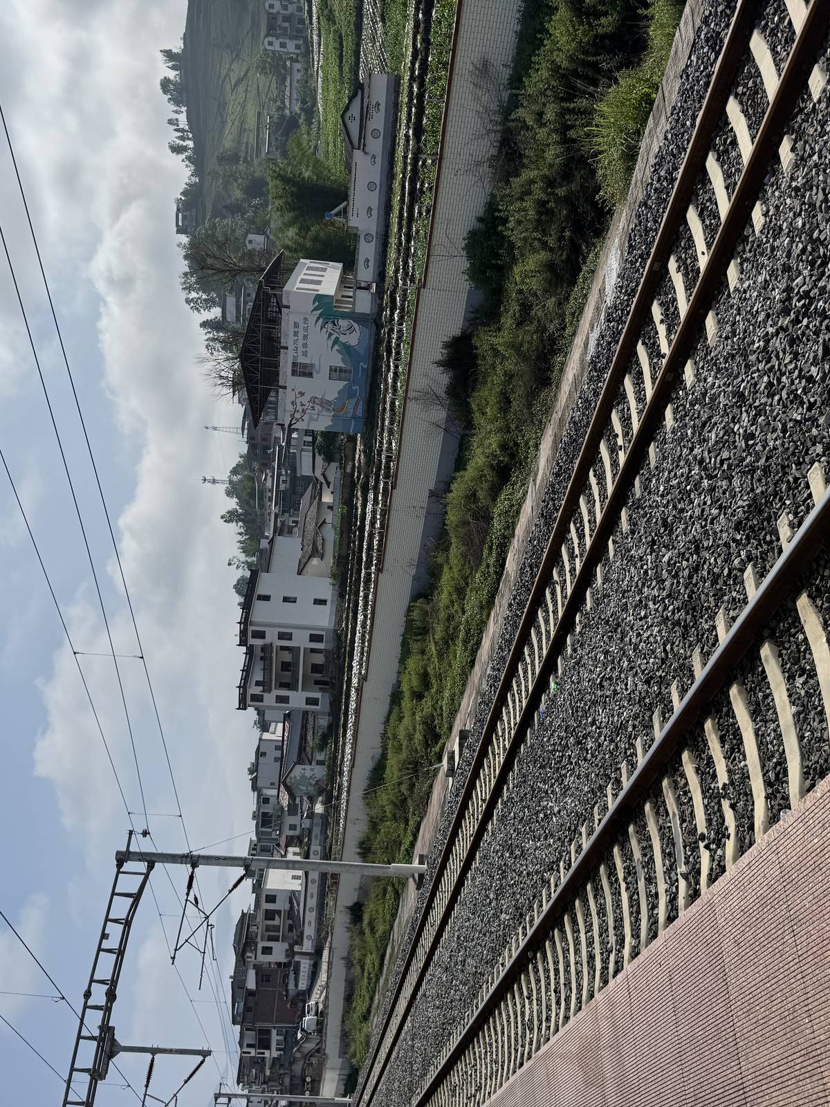轨道向远方延伸，红褐色地砖站台、远处乡镇村庄、田野与山丘